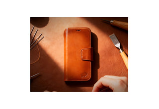 BlackBrook brown leather folio iPhone case resting on a workbench with hand-stitching tools and warm light highlighting the craftsmanship.