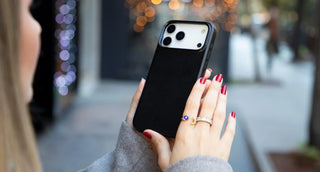 A picture of a woman holding her iPhone 17 Pro in a street.