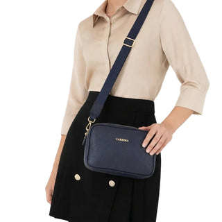 Woman wearing a navy crossbody bag with a visible brand name on a white background