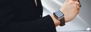 A hand model wearing a black blazer is displaying the BlackBrook Case Holo Strap for the Apple Watch on his wrist while holding glasses.